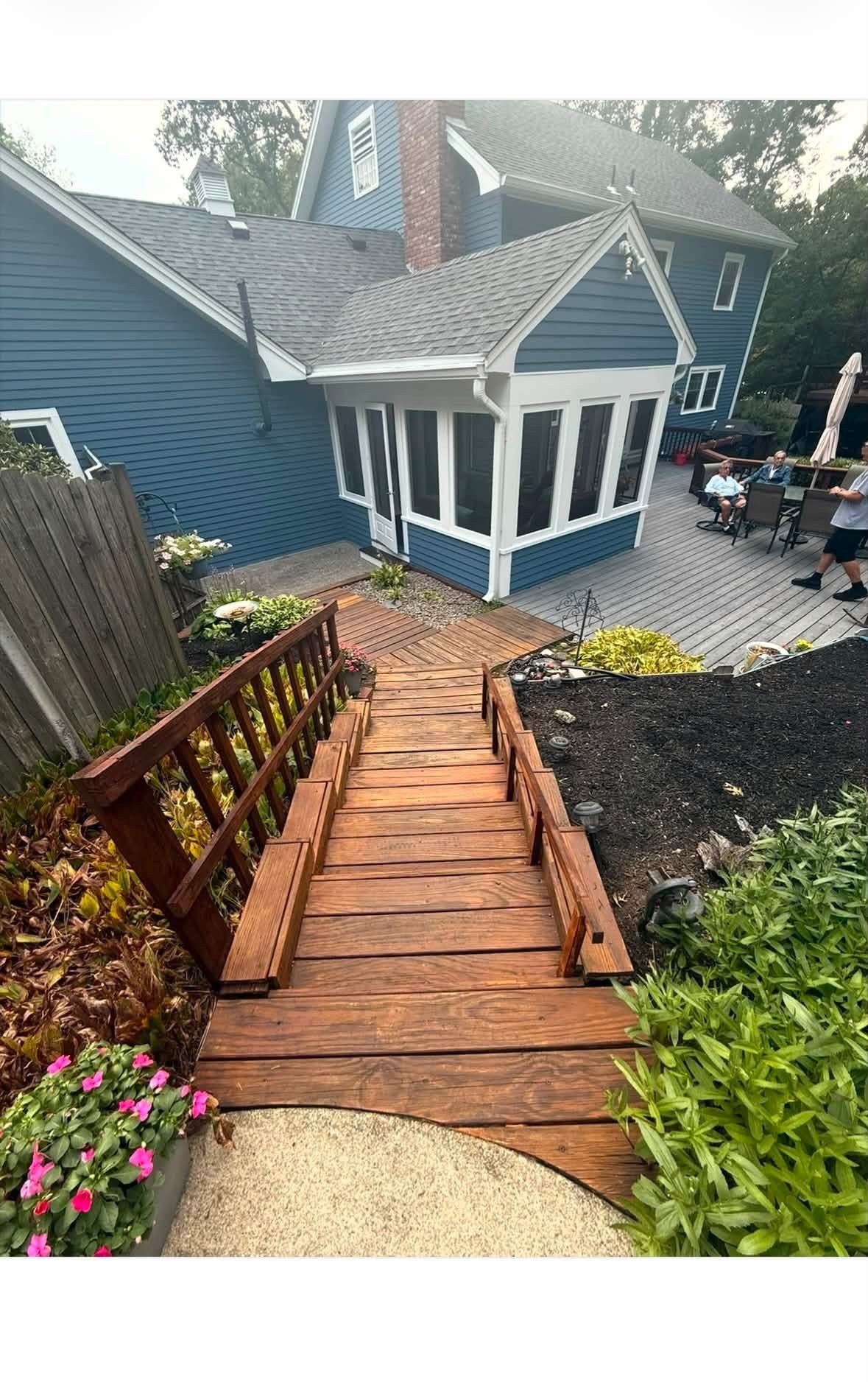 Stained wooden deck stairs and walkway leading to a blue-shingled home