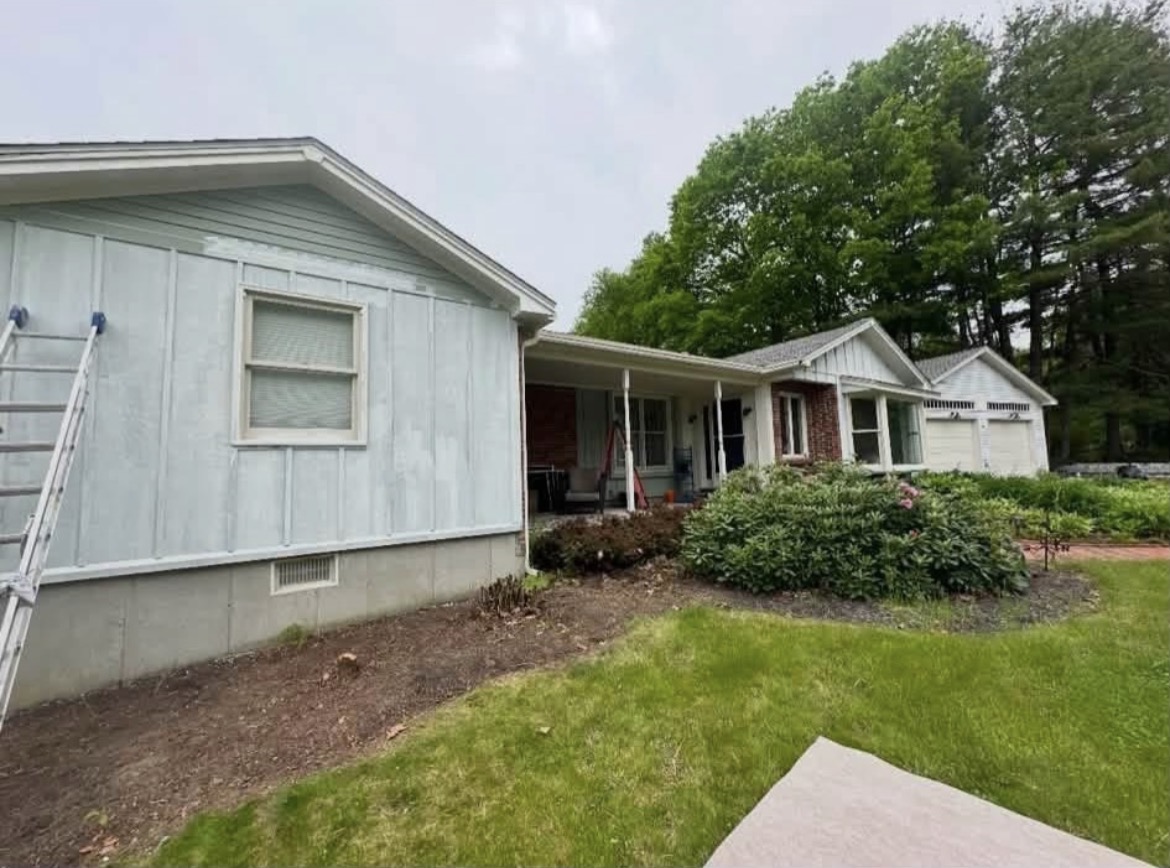 Ranch home with faded, chalky light blue siding and a ladder against the wall before painting