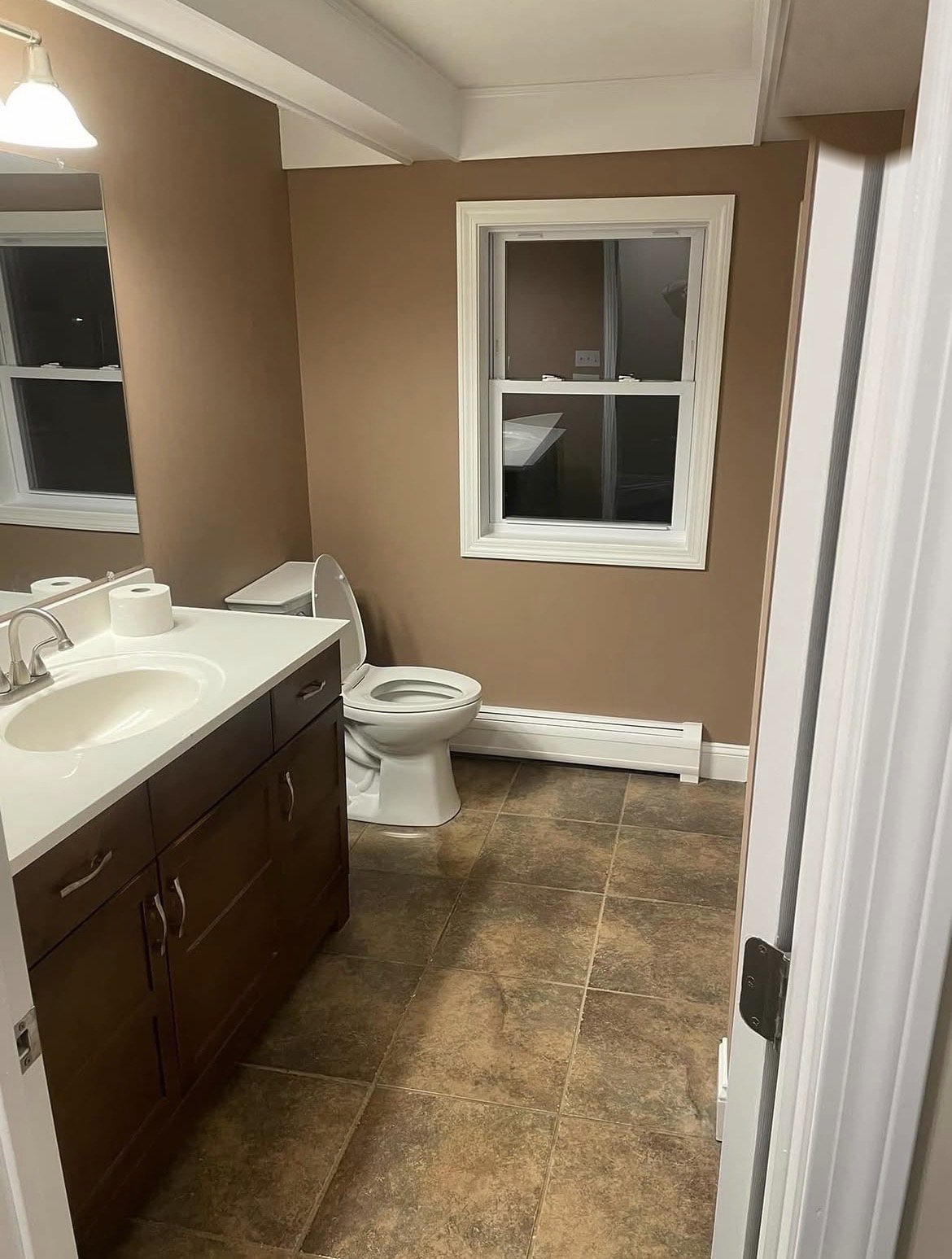 Bathroom with dated brown walls, a dark vanity and older flooring before repainting
