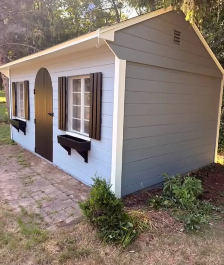 Rebuilt and painted shed with light blue and gray siding, an arched door, shutters and planter boxes
