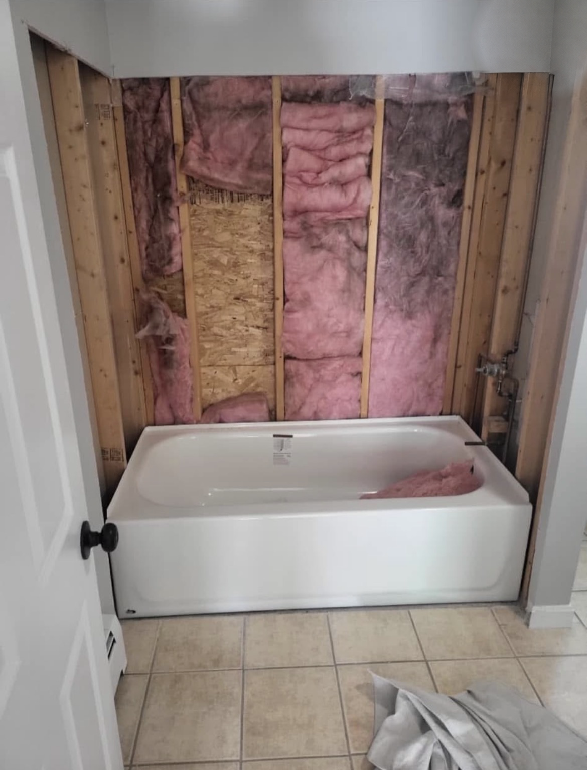 Bathroom stripped to the studs with a new tub set in place and insulation exposed during the remodel