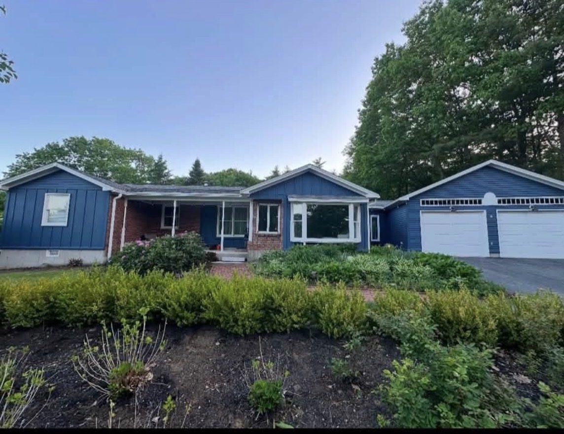 Same ranch home freshly painted deep navy blue with white trim, garage doors and brick accents