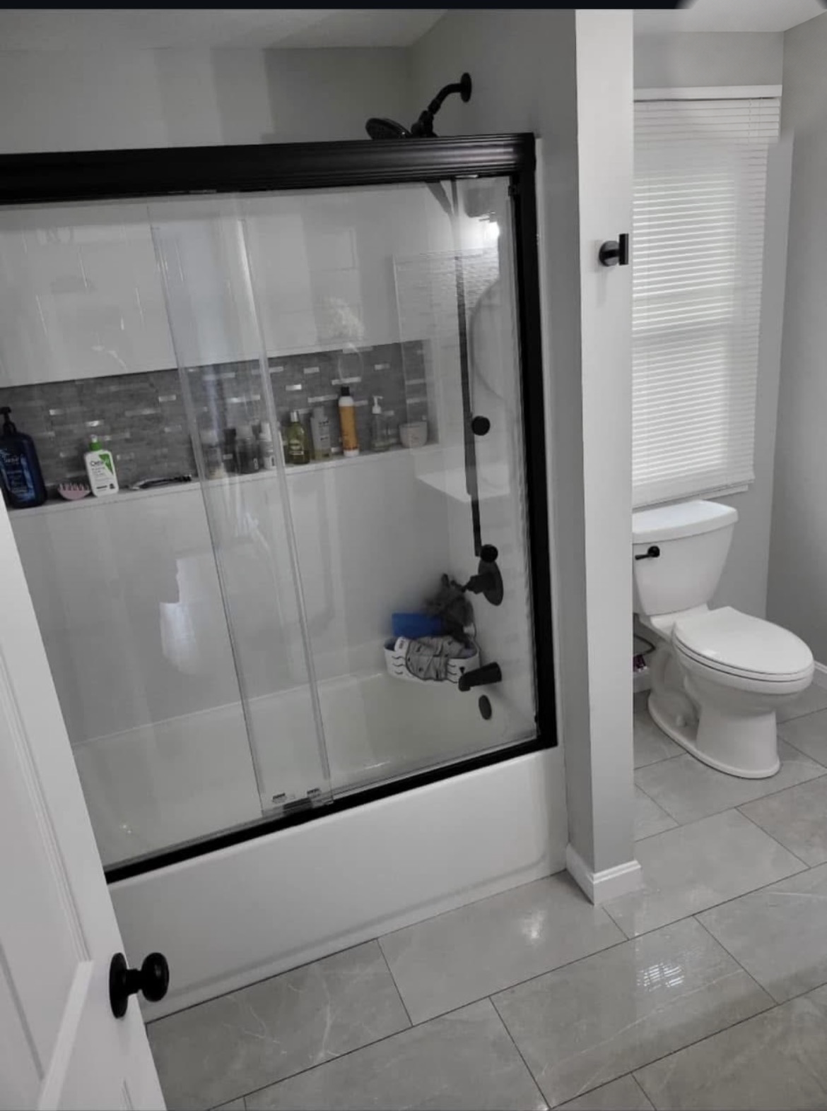 Finished bathroom with a tiled tub surround, mosaic accent niche, glass sliding doors and black fixtures