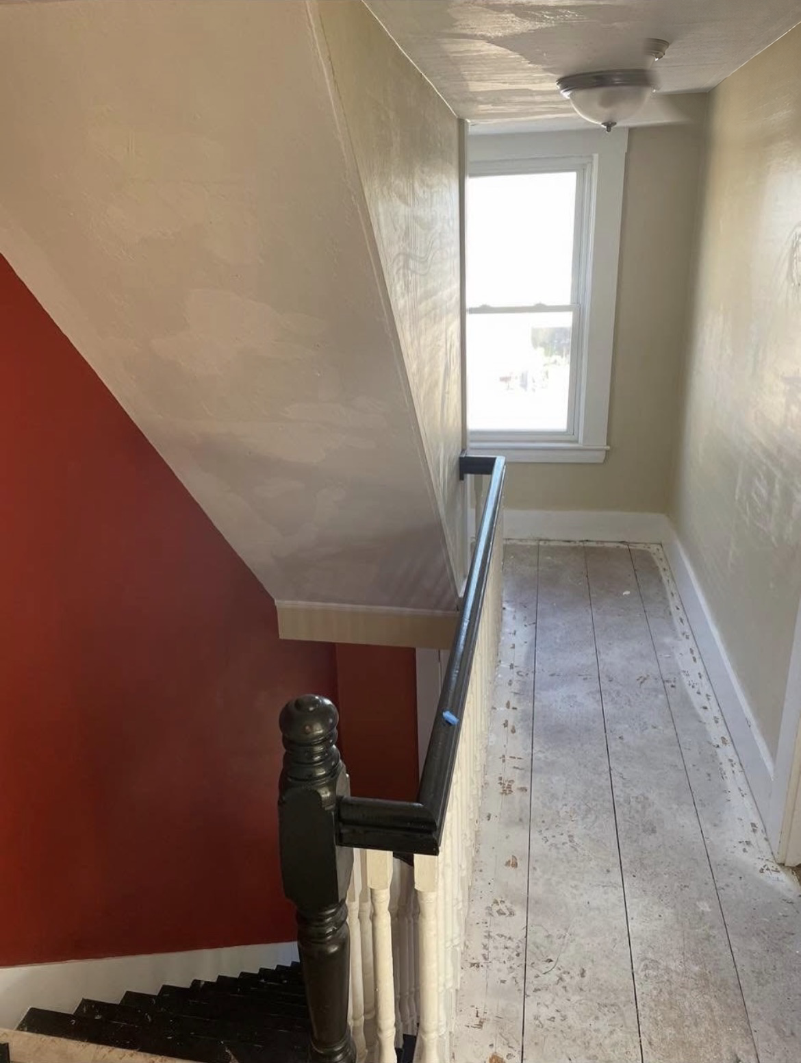 Upstairs hallway and stairwell with patched plaster walls, a red accent wall and worn painted floors before renovation